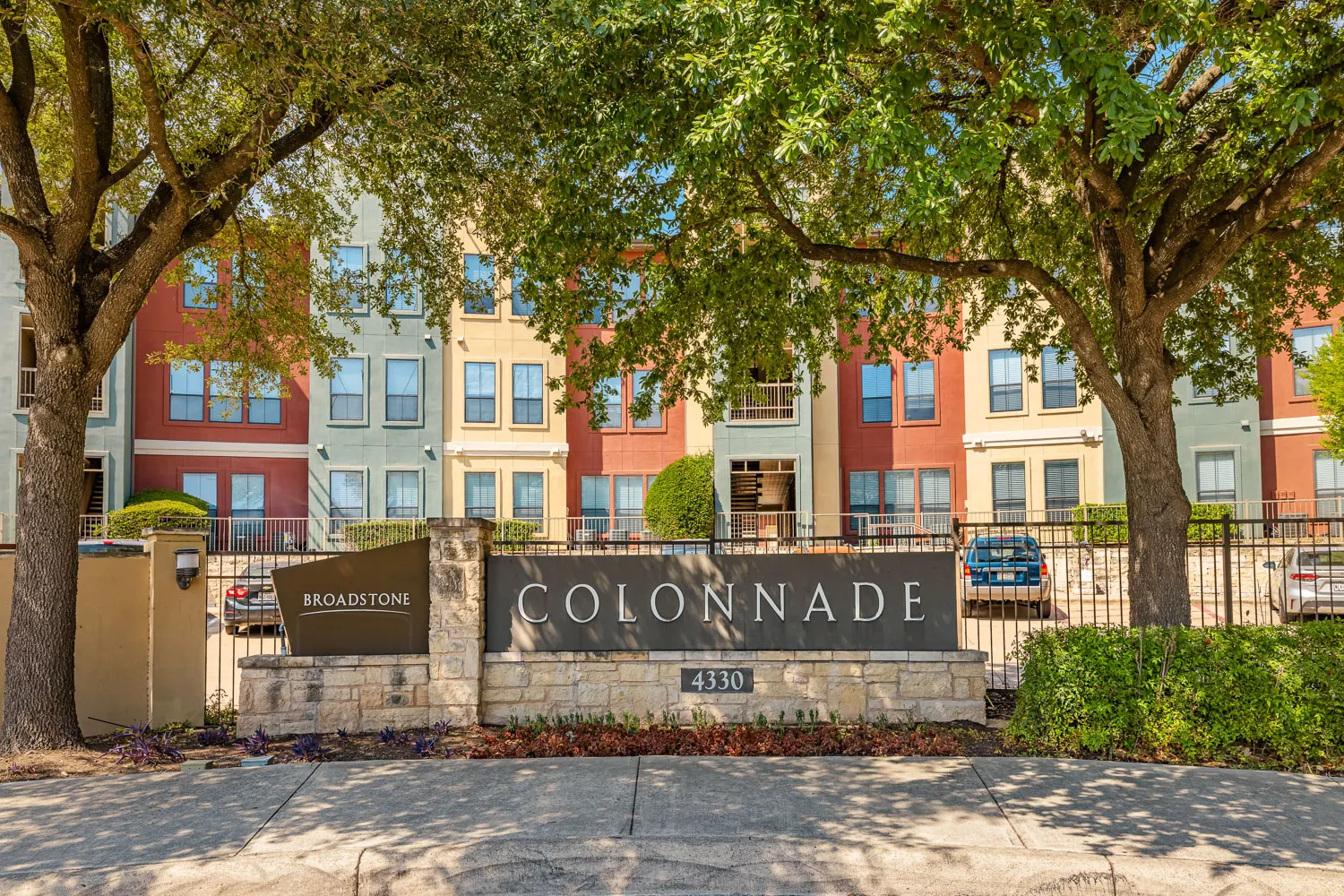 Exterior view of the Colonnade apartments with a stone sign and landscaped trees.
