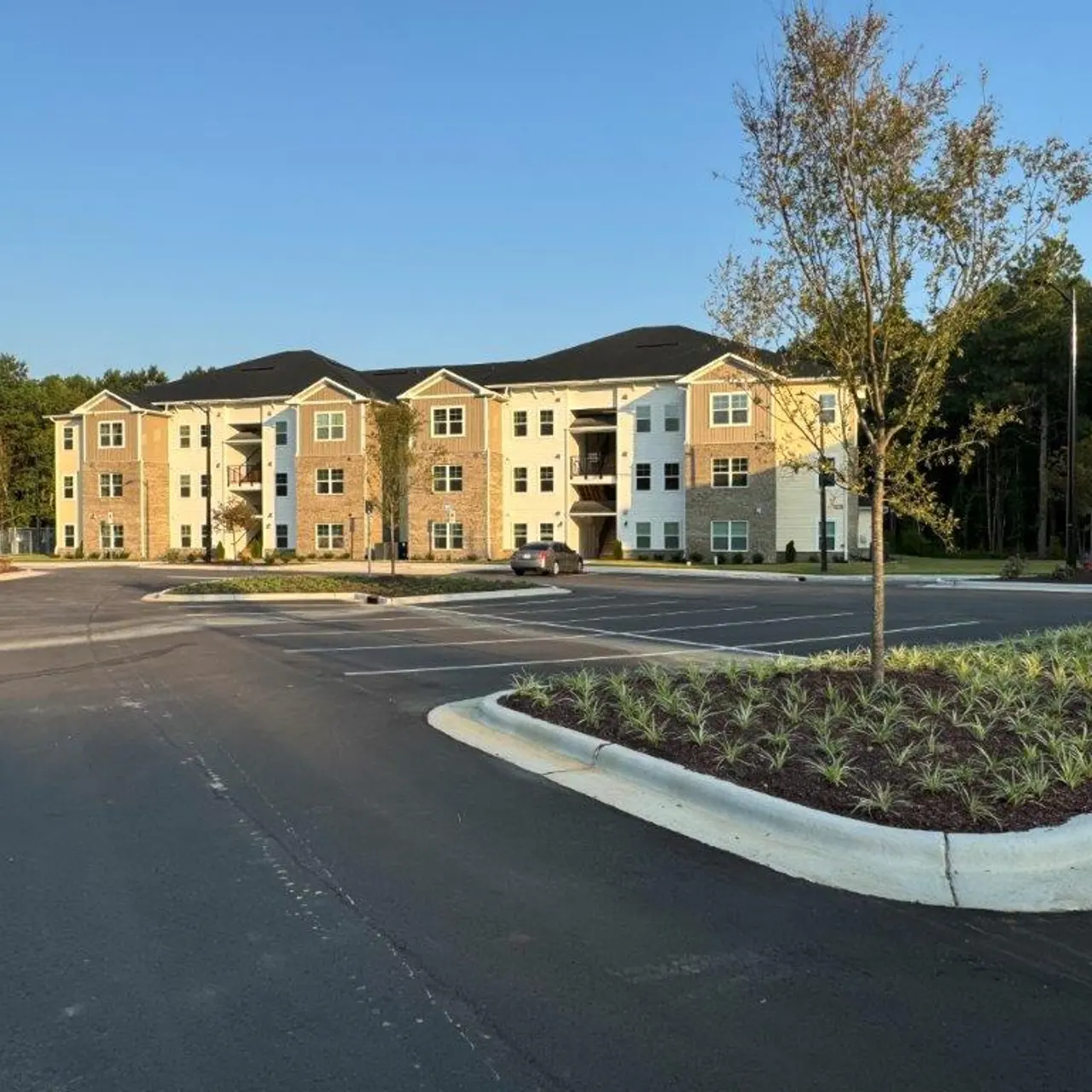 A modern three-story apartment building with landscaped grounds and a parking lot in the foreground.