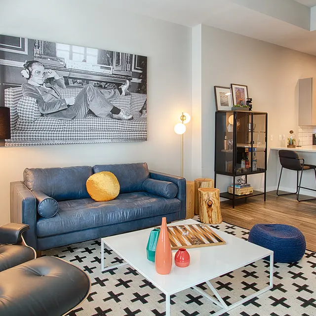 A modern living room featuring a blue sofa, a stylish armchair, a coffee table, and a large wall art with a monochrome image.