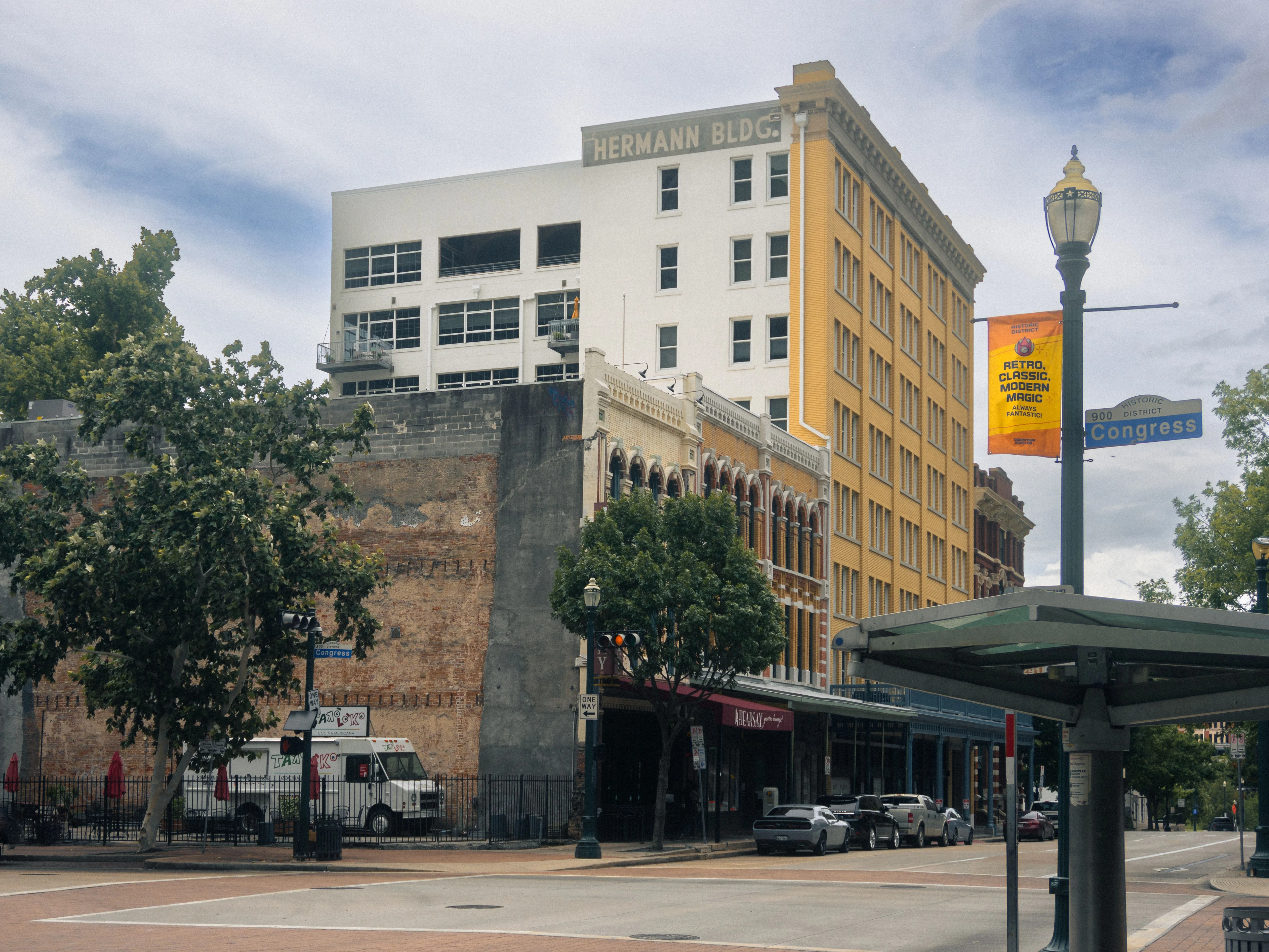 A view of the Hermann Building and surrounding streets with trees and parked cars.