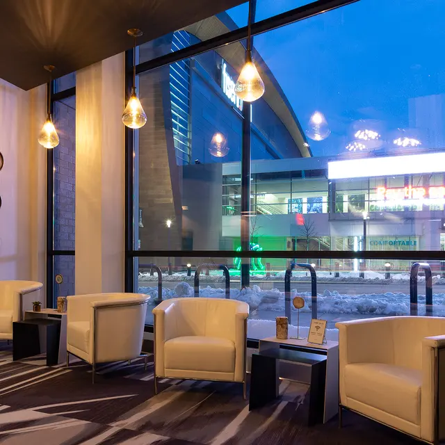 A modern lobby with white chairs and pendant lights, featuring large windows showing a nighttime city view.