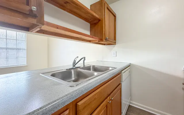 A view of a small kitchen with wooden cabinets, a double sink, and a dishwasher.