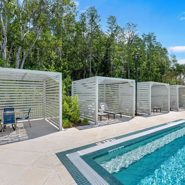 Modern Pool Area with Cabanas A modern pool area featuring several shaded cabanas and a blue swimming pool surrounded by greenery and trees.