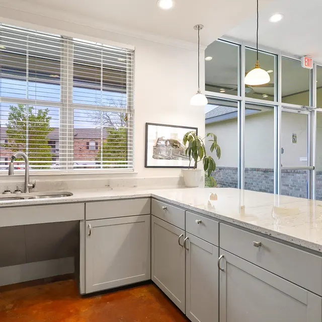 Modern kitchen interior featuring gray cabinets, a sink, and large windows allowing natural light.