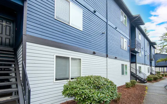 Exterior view of a modern, multi-story apartment building featuring blue and white siding, surrounded by landscaping.