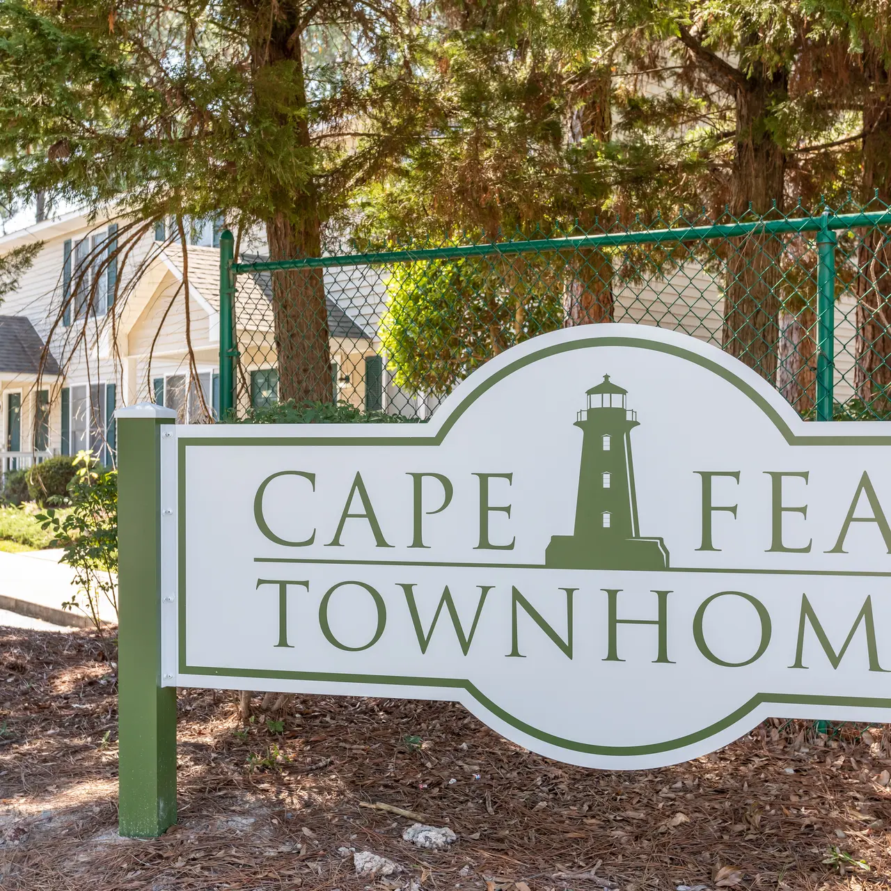Sign for Cape Fear Townhomes with a lighthouse design, surrounded by trees.