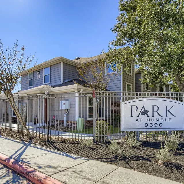 Exterior view of Park at Humble featuring a gated entrance, green landscaping, and a blue sky in the background.