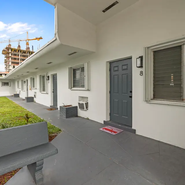 Exterior view of an apartment complex courtyard with a central lawn and unit doors.