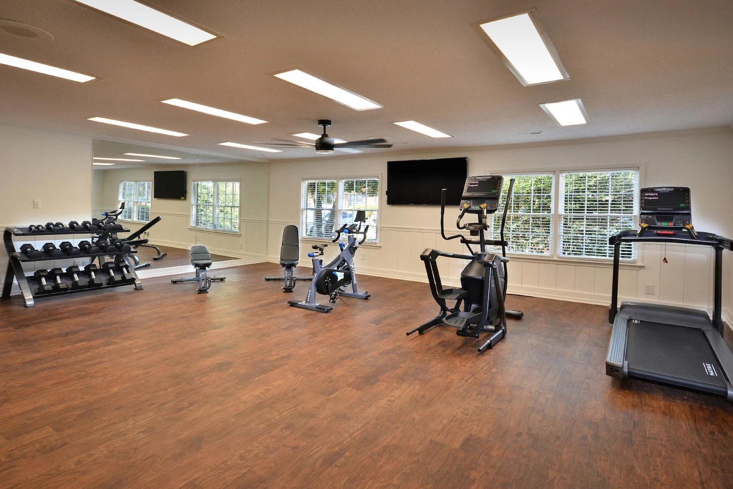 Modern Gym Interior A modern gym interior featuring exercise equipment including dumbbells, a stationary bike, a treadmill, and an elliptical machine, with large windows letting in natural light.