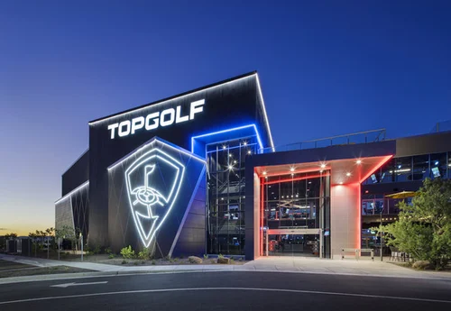 Exterior view of a Topgolf location at dusk, featuring a modern design with illuminated signs and colorful lighting.
