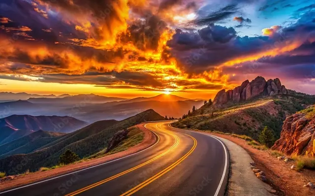 A winding road through mountainous terrain at sunset, with dramatic clouds and vibrant colors in the sky.