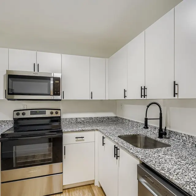 A modern kitchen featuring white cabinetry, a black stove, a built-in microwave, and granite countertops with a sink.