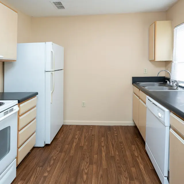 A modern kitchen featuring light wooden cabinets, a black countertop, and stainless steel appliances including a refrigerator, stove, and dishwasher.