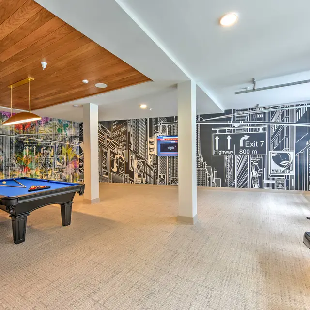 A modern game room featuring a blue pool table, wooden ceiling, and graphic mural on the wall.