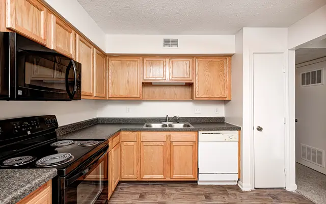A modern kitchen featuring wooden cabinets, black appliances, and a gray countertop.