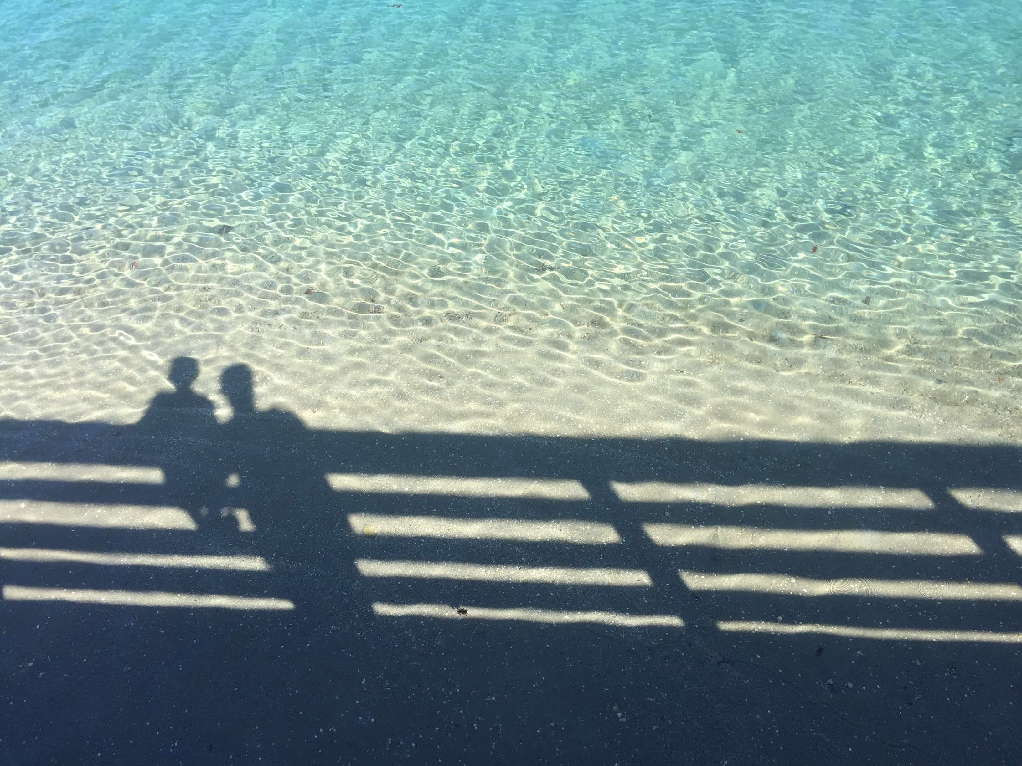Shadows of two people sitting on a pier with the ocean below.