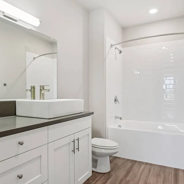 Contemporary Bathroom Design A modern bathroom featuring a white vanity with a rectangular sink, a large mirror, a shower-tub combination, and wooden flooring.