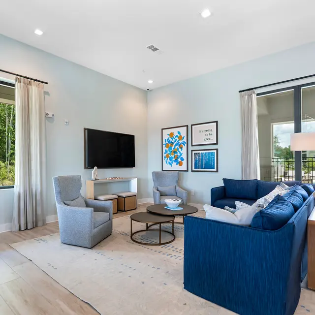 Modern Living Room Design A modern living room with a blue sofa, two gray armchairs, a round coffee table, and a mounted TV on the wall. The space features large windows with light curtains and decorative wall art.