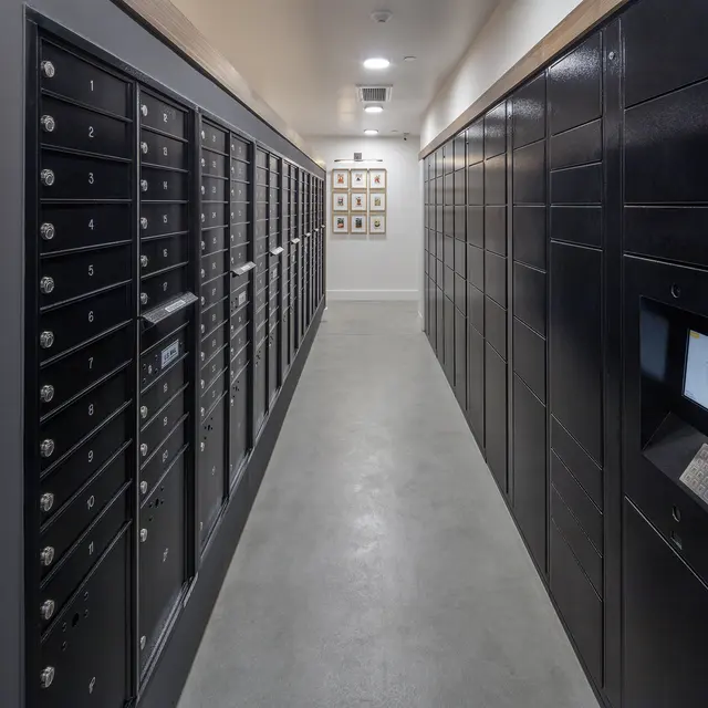 An indoor mailroom featuring rows of black and metal mail lockers along a narrow corridor.
