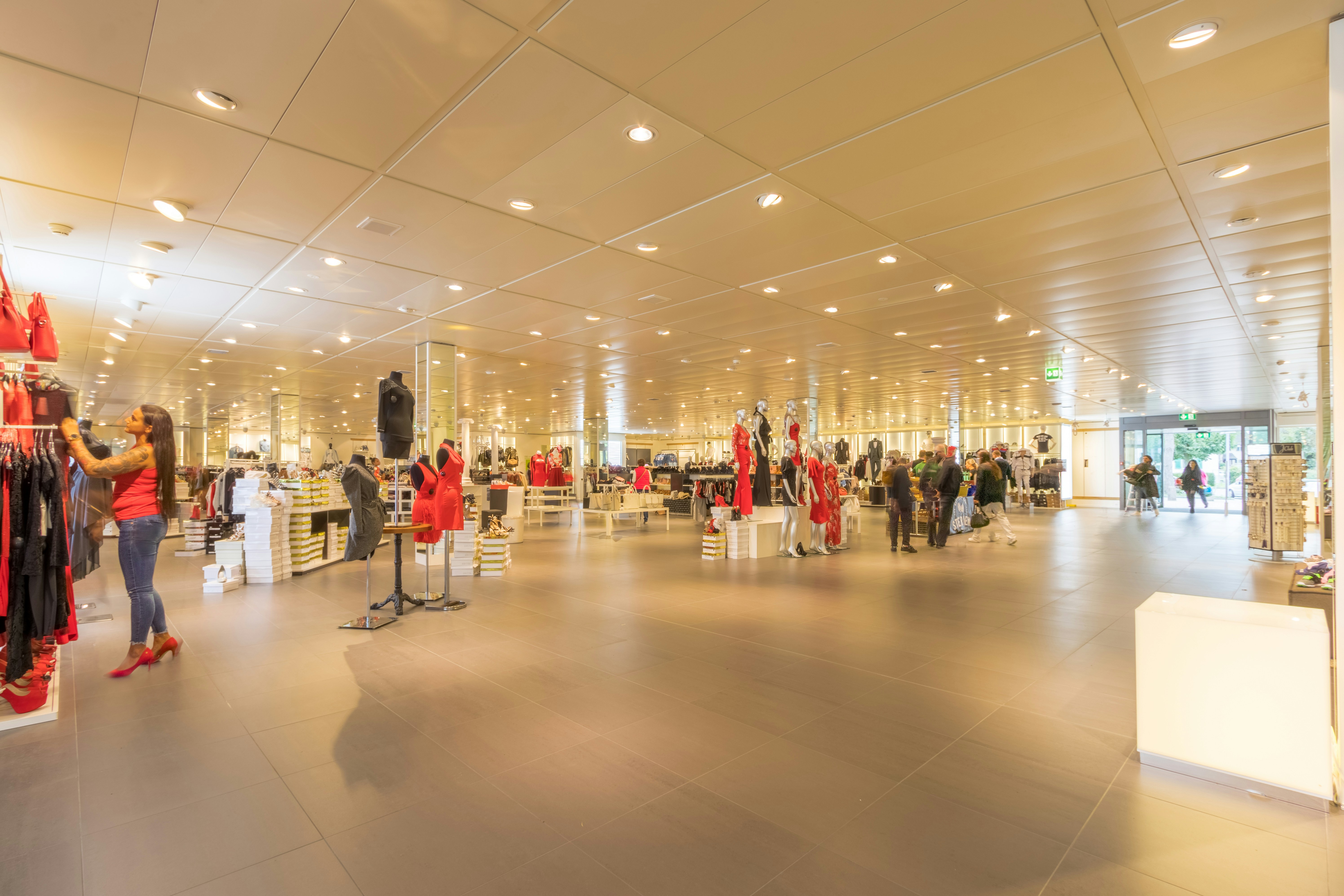 Interior view of a modern clothing store featuring clothing racks and displays, with shoppers browsing and trying on clothes.