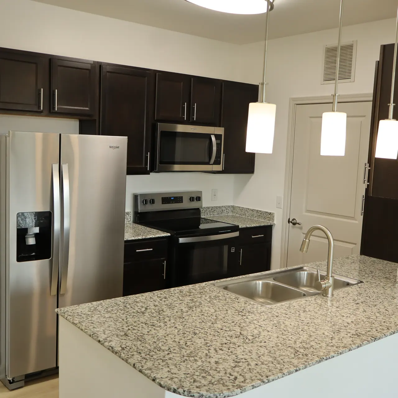 A modern kitchen featuring dark wood cabinets, sleek stainless steel appliances, and a granite countertop with a double sink.