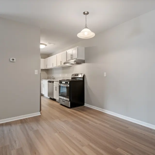A modern kitchen in an apartment featuring light colored cabinetry, stainless steel appliances, and wooden flooring.
