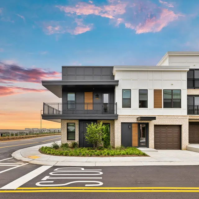 Modern Residential Building at Sunset A modern building exterior with a two-toned facade—white and dark gray—featuring balconies and large windows, situated at a street corner with a dramatic sunset sky.