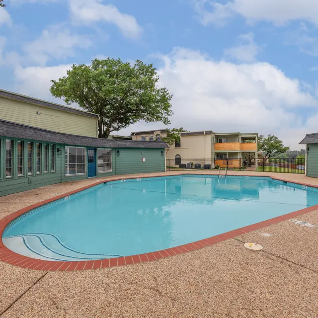 The Hills - A tranquil swimming pool area surrounded by buildings, featuring a clear blue pool and patio space on a cloudy day.
