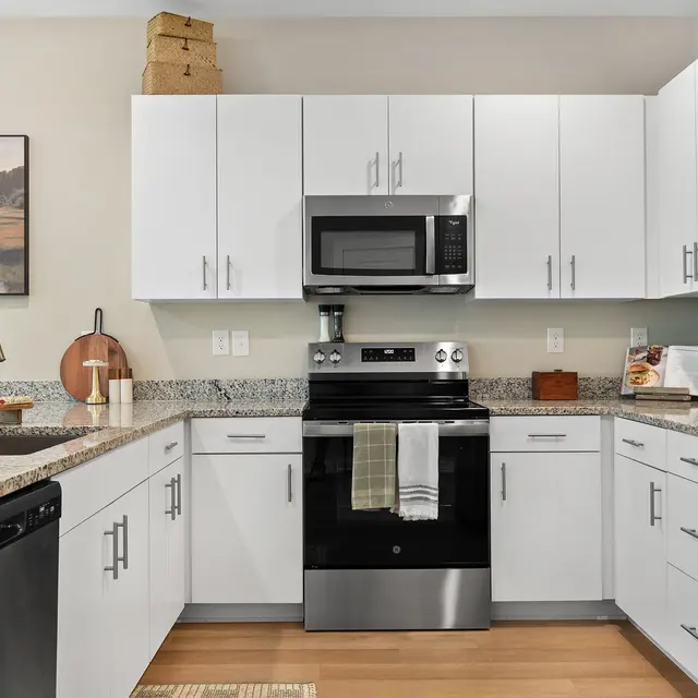 A modern kitchen featuring white cabinetry, stainless steel appliances, and granite countertops. The kitchen has a black stove, microwave, and a casual dining setting.