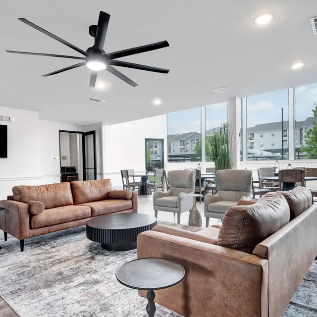 Stylish Modern Living Area A stylish modern living area with brown leather sofas, a round coffee table, and large windows letting in natural light. A ceiling fan is visible. The decor features a light rug and a dark wooden floor.