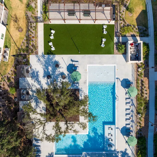 Aerial view of a modern apartment complex featuring a swimming pool, cabana, and green lawn area.