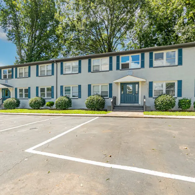 Exterior view of a two-story apartment building with blue shutters and manicured landscaping
