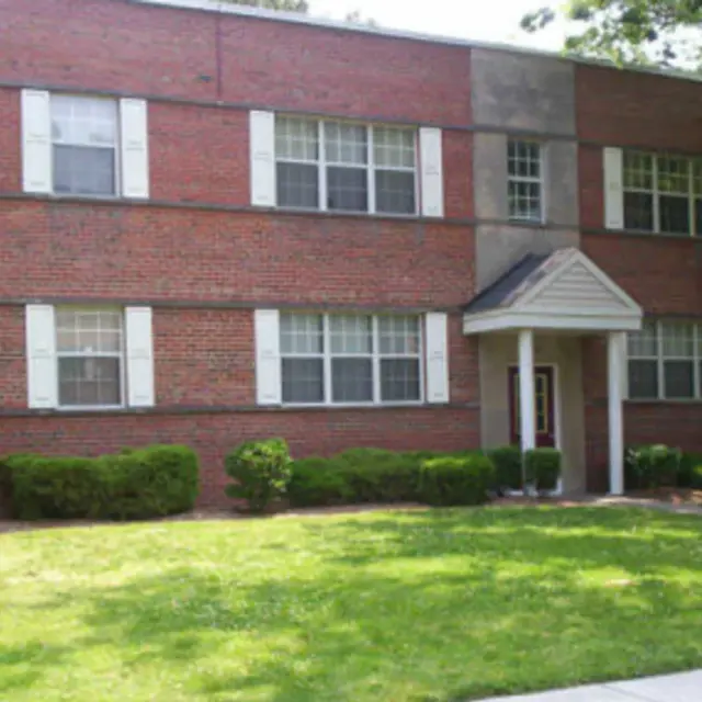 Exterior view of a red brick apartment building with white accents and a well-maintained lawn.