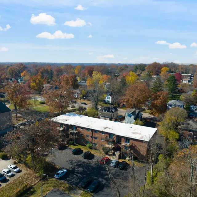 Aerial view of a housing complex surrounded by trees with autumn foliage and parked cars.