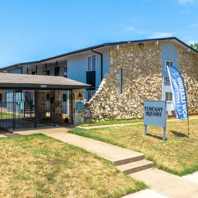 Exterior view of Tuscany Square apartments featuring a stone structure and a gated entrance with a sign.