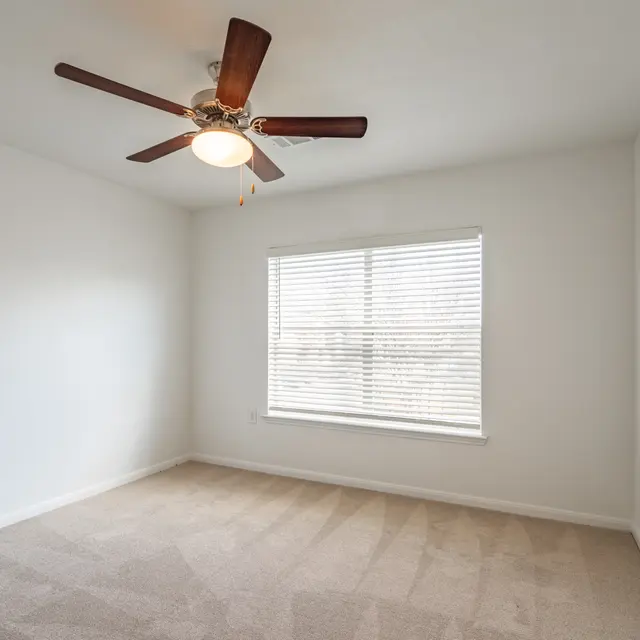 A vacant room with a ceiling fan and a window.