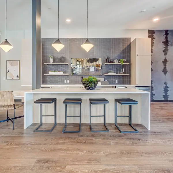 Modern kitchen with a large island, high stools, and minimalist decor, featuring a stylish backsplash and natural wood flooring.