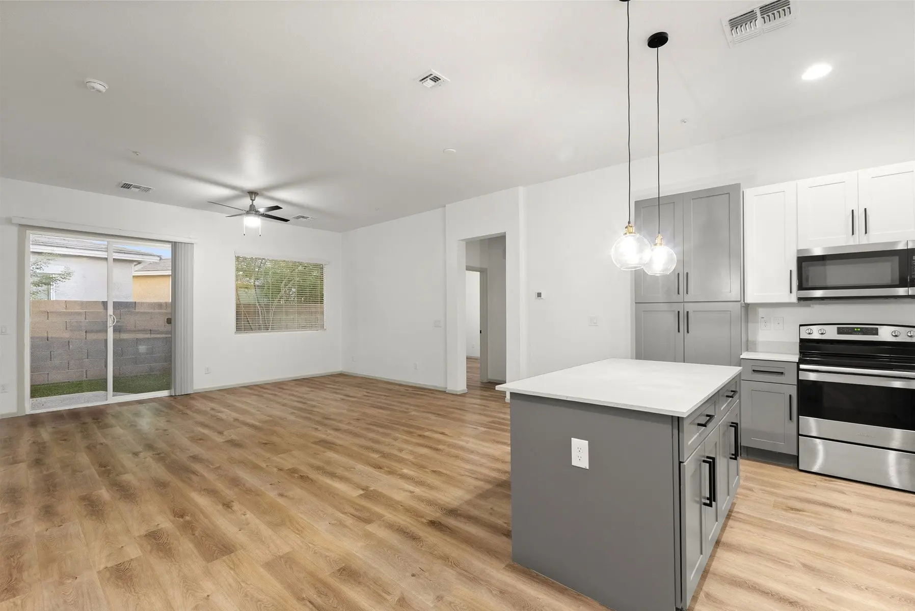 Modern kitchen and living area with light wood floors, stainless steel appliances, large window, and pendant lighting.