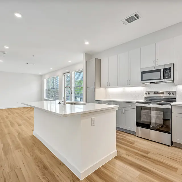 Modern Open Concept Kitchen A modern kitchen with white cabinets and stainless steel appliances, featuring an island with a sink and wooden flooring.