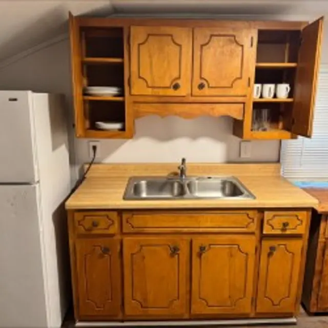 A small kitchen area featuring wooden cabinetry and a double sink with a countertop.