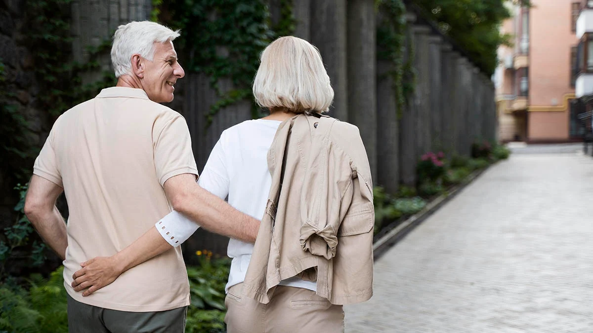 Senior Couple Walking Together A senior couple walking hand in hand down a pathway surrounded by greenery.