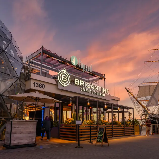 The Brigantine seafood restaurant at sunset with a tall ship in the background.