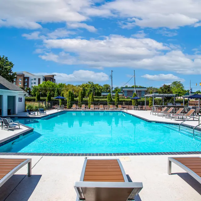 A bright outdoor swimming pool surrounded by lounge chairs under a clear blue sky.