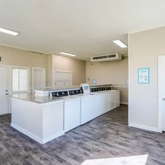 Interior view of a laundry facility with multiple washing machines and dryers against a white wall.