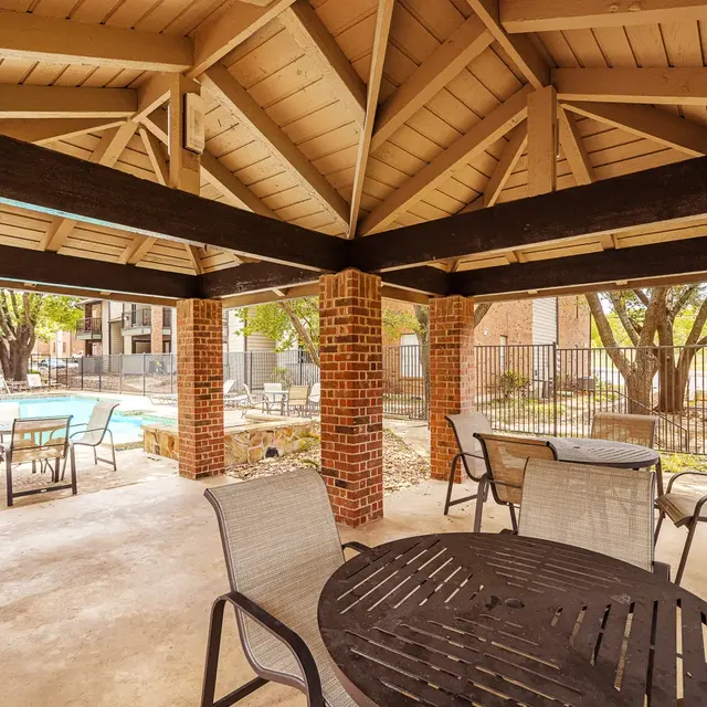 Covered seating area near a pool with tables and chairs