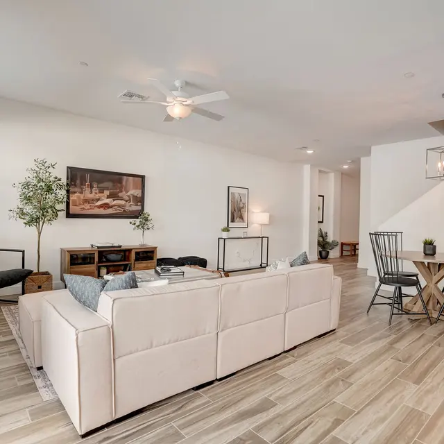 Contemporary Living Room Design A modern living room featuring a light-colored sectional sofa, a black accent chair, a wooden coffee table, and a decorative plant. There is artwork on the wall and a dining area with a round wooden table and black chairs in the background.