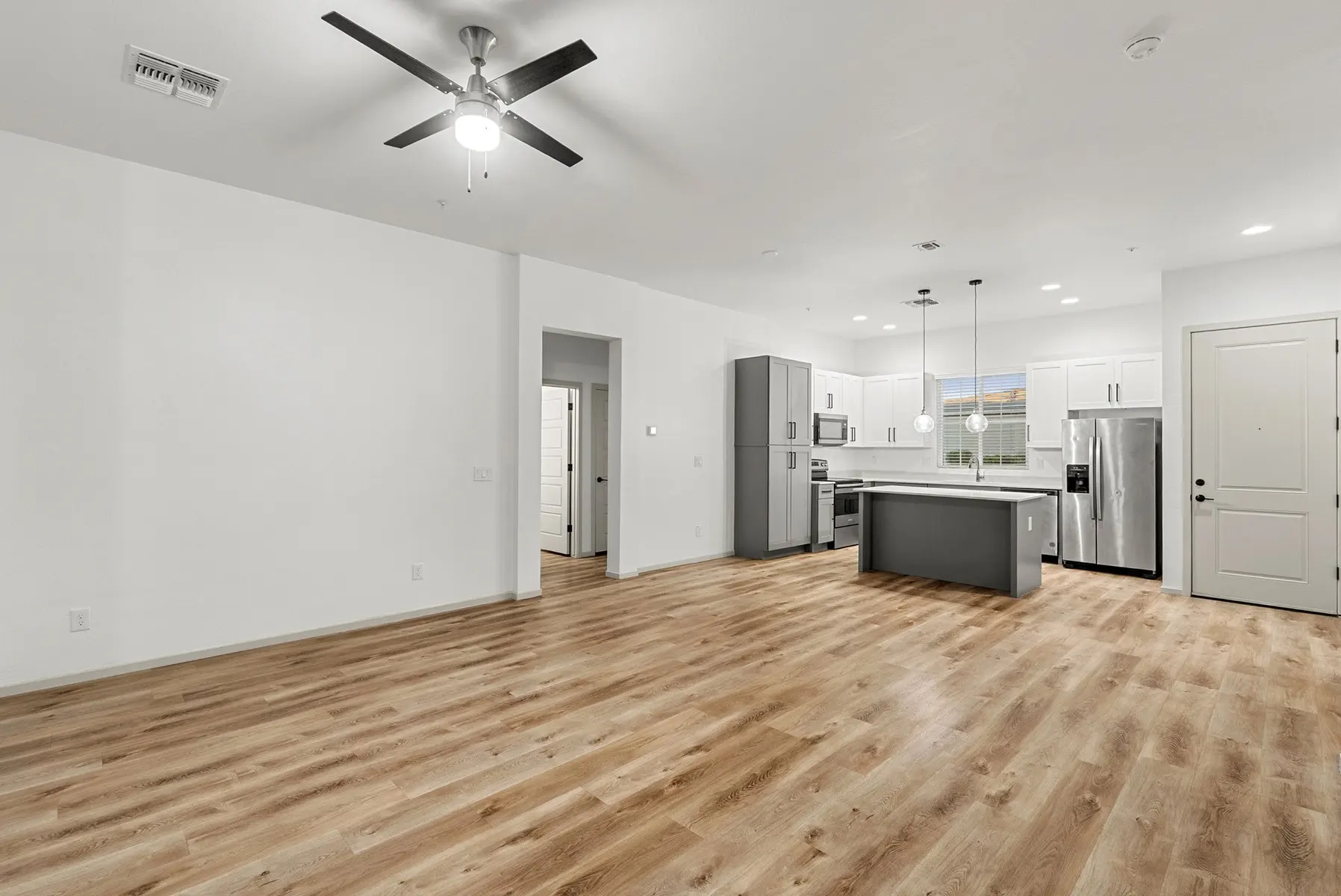 Modern open-concept living area with hardwood floors, ceiling fan, and a kitchen featuring stainless steel appliances and a large island.