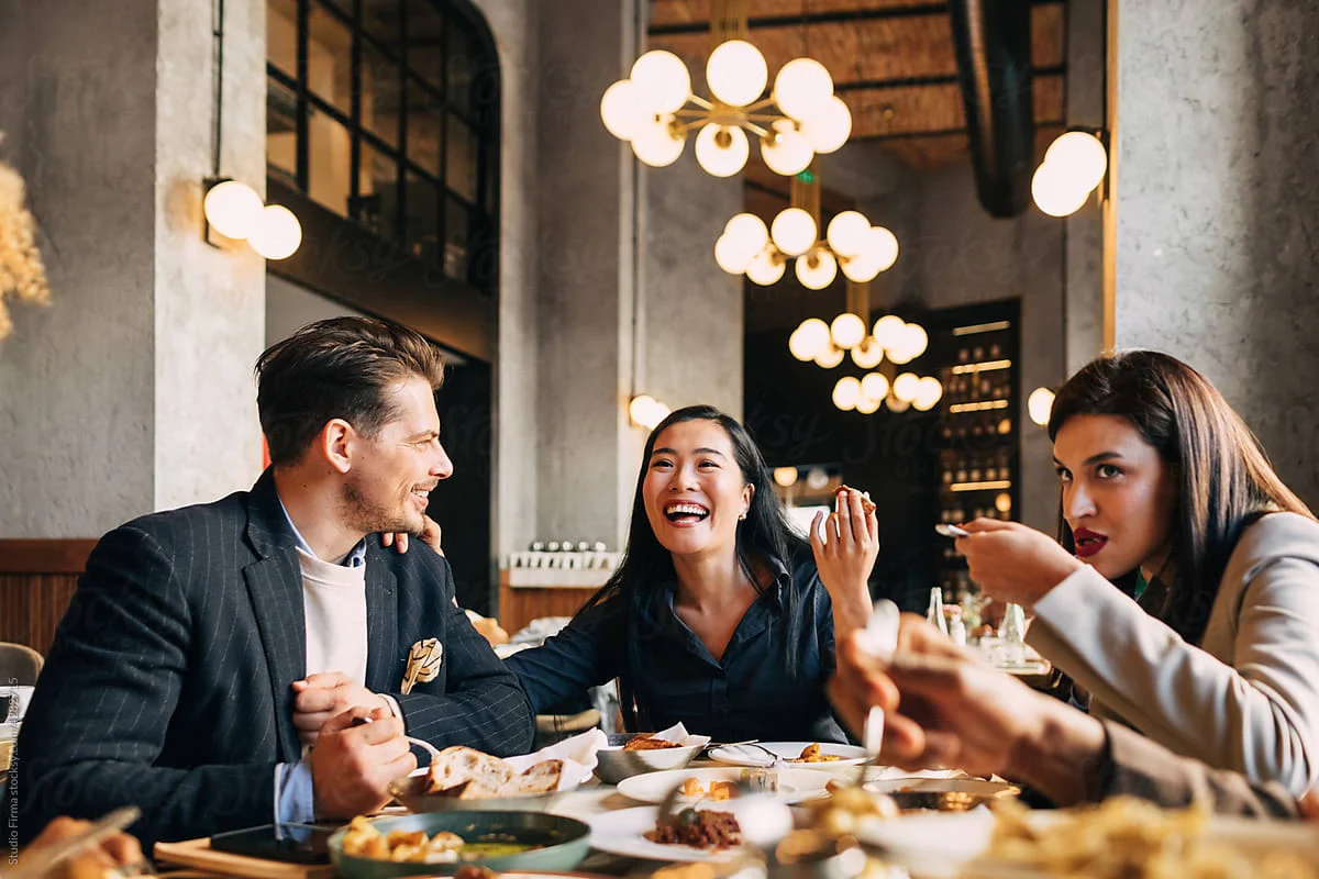 Dining with Friends: A Joyful Meal Group of friends enjoying a meal at a restaurant, laughing and engaging in conversation over a table filled with food.