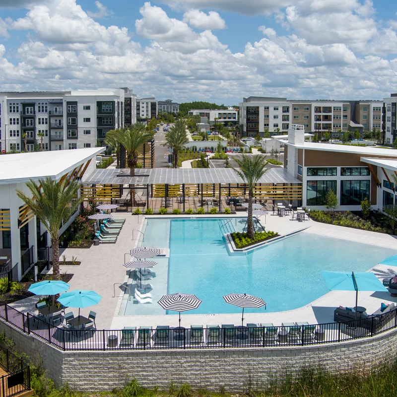Luxury Apartment Complex with Pool A modern luxury apartment complex featuring a large pool area with palm trees and lounge chairs, surrounded by buildings.