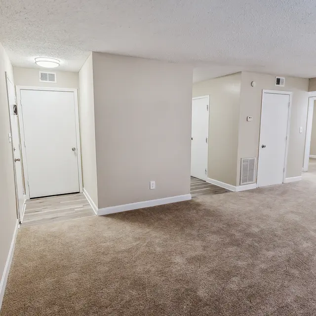 An empty apartment interior featuring beige walls, multiple doors, and carpet flooring.